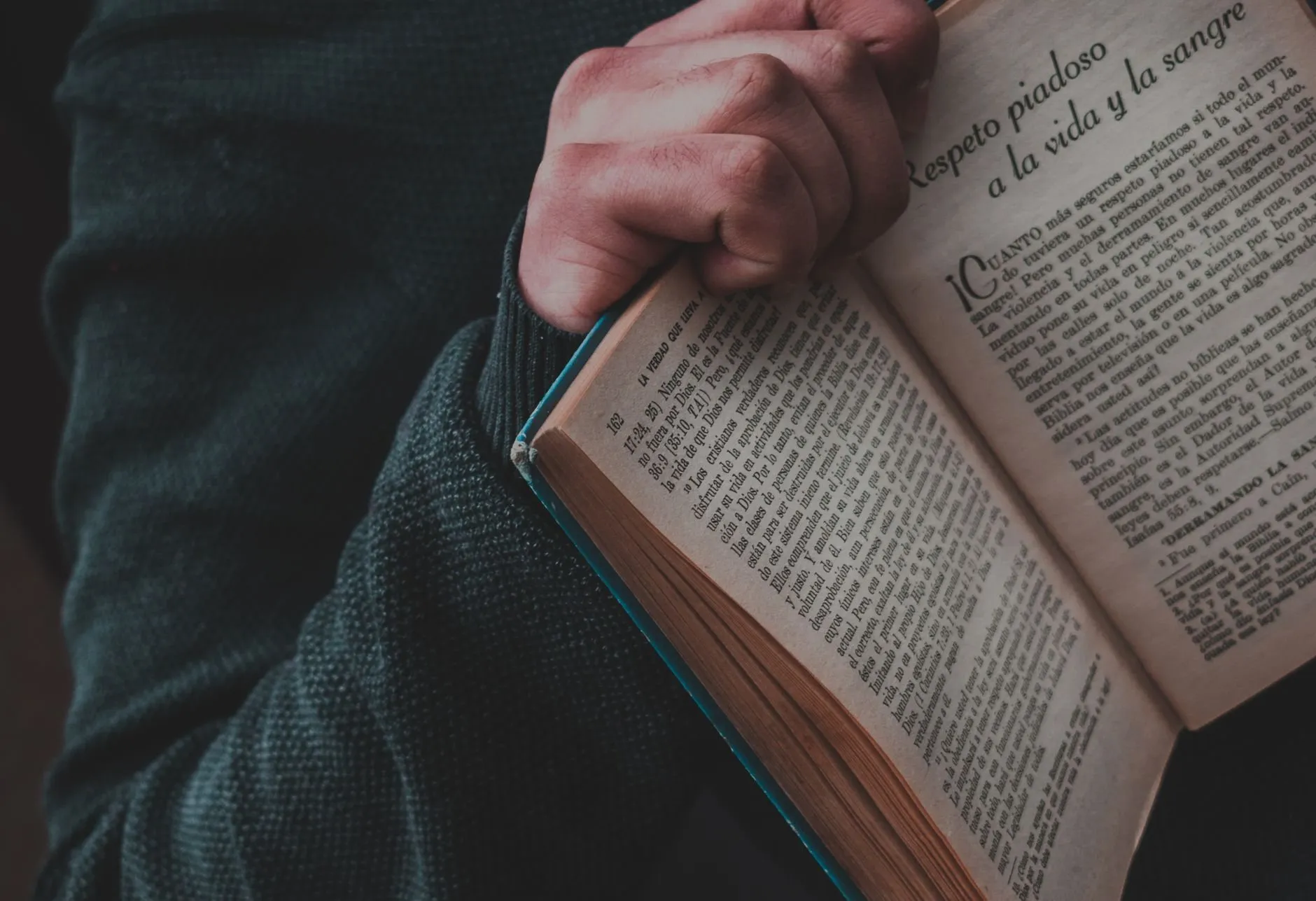 Hands holding an old book open against a dark knitted sleeve