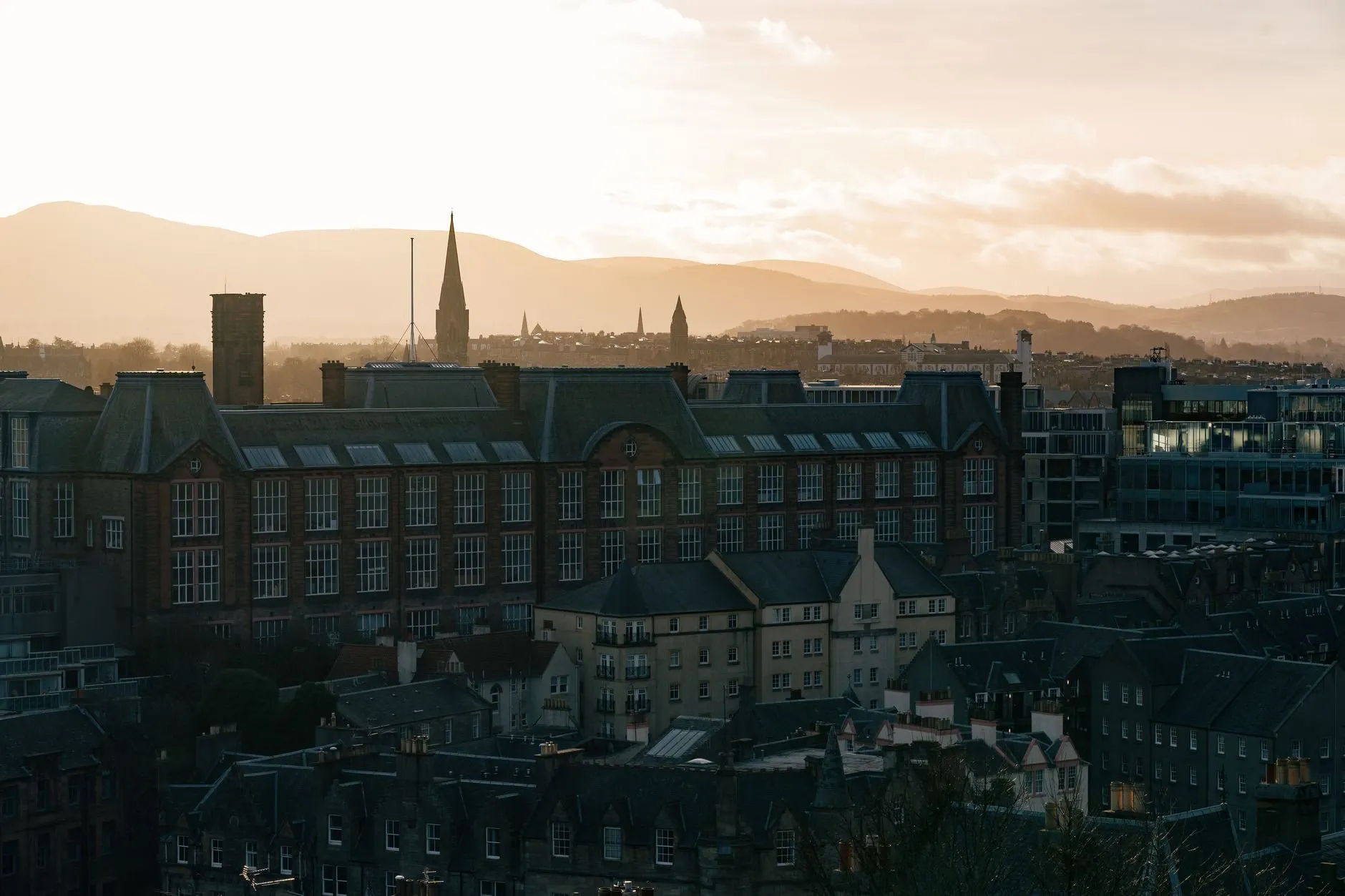 Rooftops and a church spire at first light, with hills beyond