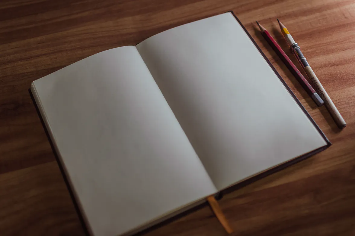 An open notebook and two pens on a dark bench, the page still blank.