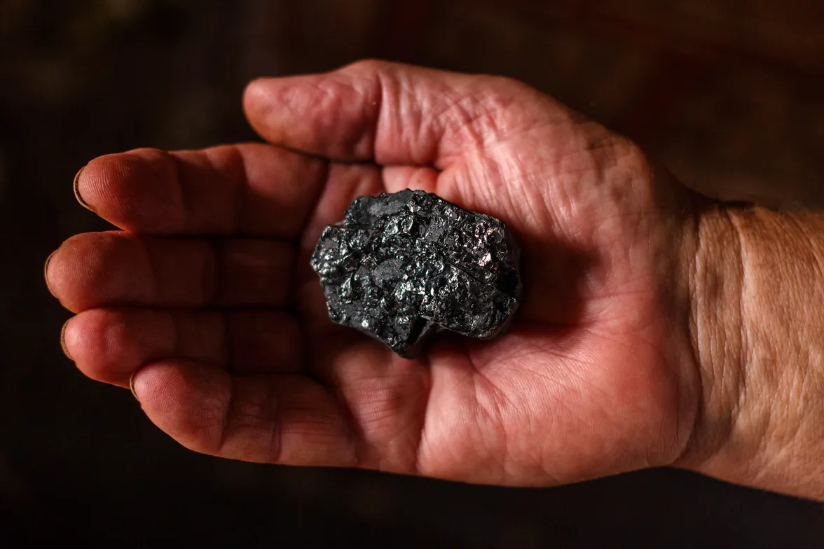 A worn hand holding a dark, glittering lump of ore the size of a walnut.