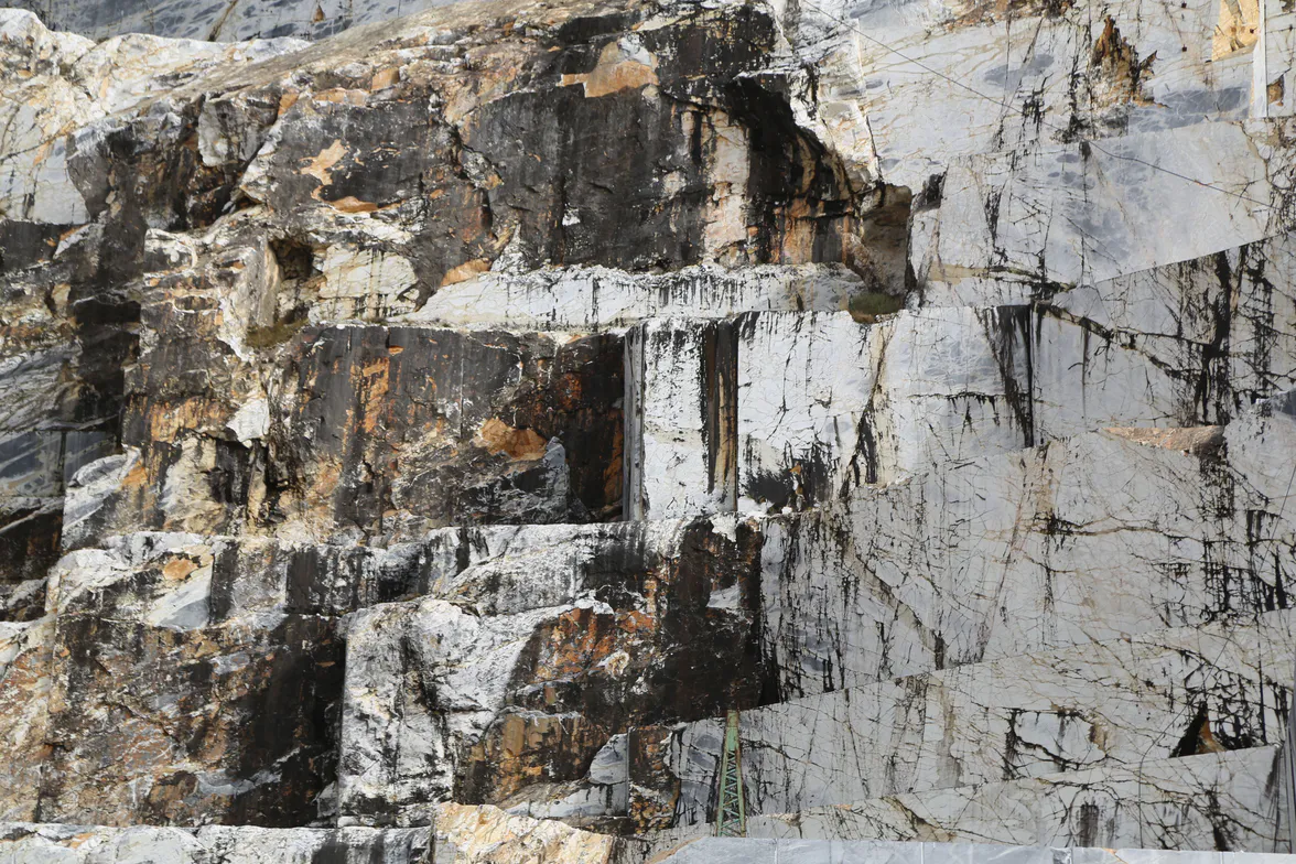 A quarry face of pale banded rock, cut square, with dark seams running through it.