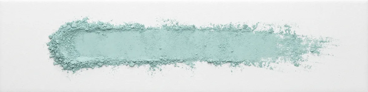 A broad horizontal smear of pale blue-green powder drawn across a white porcelain streak plate.