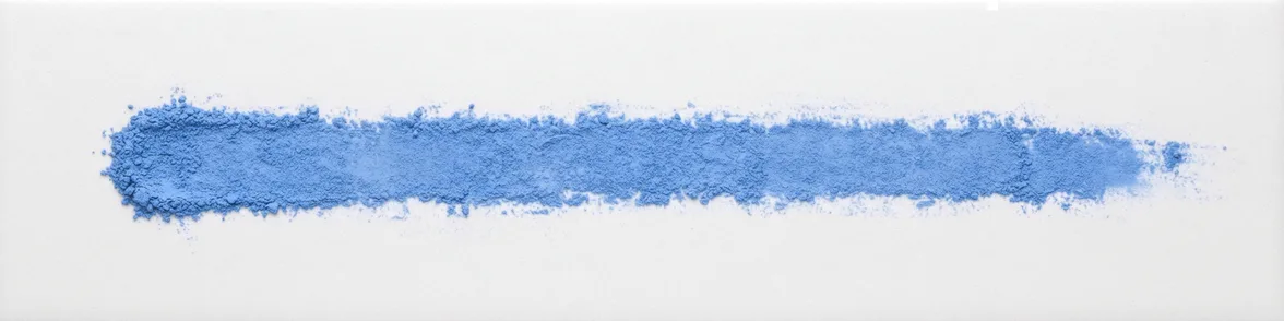 A broad horizontal smear of pale blue powder drawn across a white porcelain streak plate.