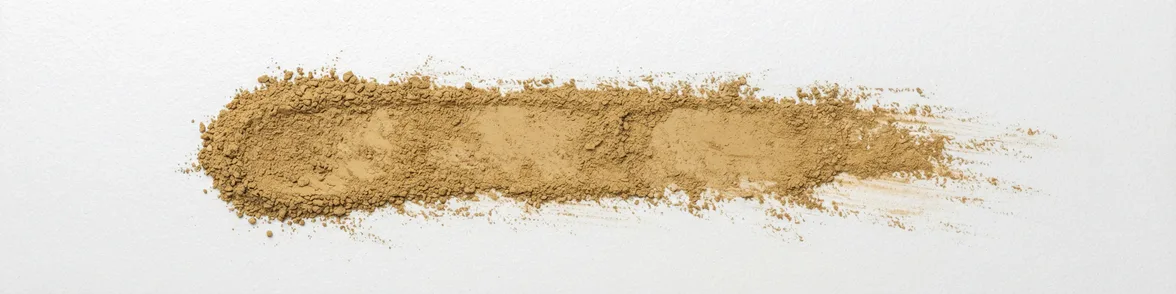A broad horizontal smear of yellow-brown powder drawn across a white porcelain streak plate.