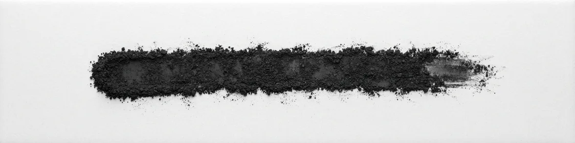 A broad horizontal smear of black powder drawn across a white porcelain streak plate.