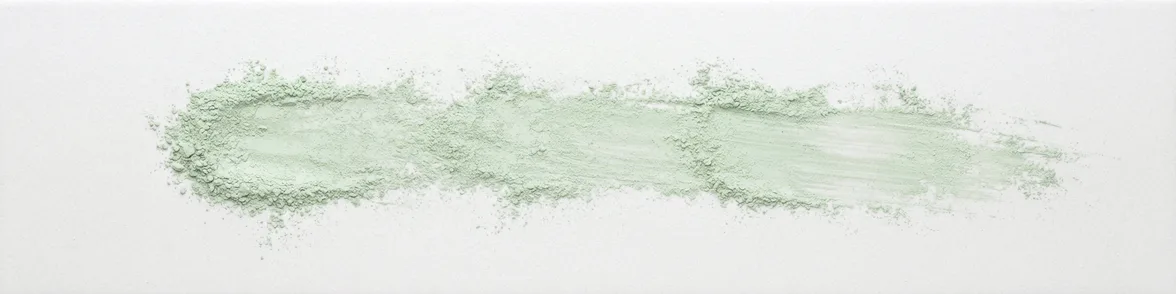 A broad horizontal smear of pale green powder drawn across a white porcelain streak plate.