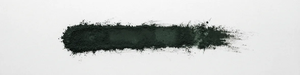 A broad horizontal smear of greenish black powder drawn across a white porcelain streak plate.